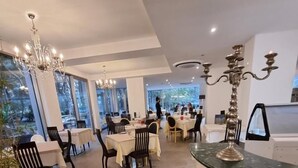 A spacious dining area with multiple tables and chairs, large windows, and a modern kitchen with a marble countertop. - Hotel Venice Beach (San Michele al Tagliamento)
