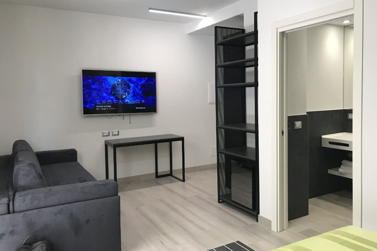 Una sala de estar moderna con una televisión de pantalla plana, un sofá, una mesita pequeña y un mueble de estanterías negro.