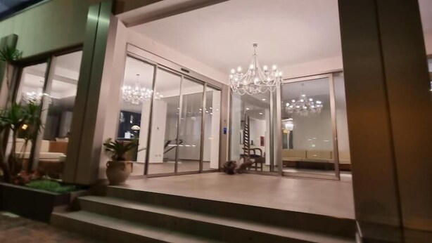 A modern building entrance with glass doors, a chandelier, and a staircase leading up. - Hotel Venice Beach (San Michele al Tagliamento)