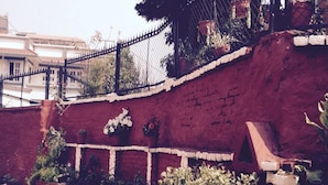 A red brick wall with a white railing, potted plants, and a black metal fence. - Dev Guest House (Lalitpur)