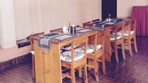 A dining area with wooden tables and chairs, a patterned table runner, and a red curtain in the background. - Dev Guest House (Lalitpur)