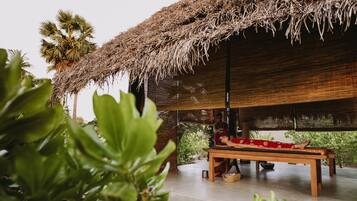 A room with a thatched roof, a wooden bench, and a view of greenery.