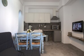 Eine kompakte Küche mit weißen Schränken, einer Mikrowelle und einem kleinen Kühlschrank. Ein Esstisch mit Stühlen und ein an der Wand montierter Fernseher sind ebenfalls vorhanden.