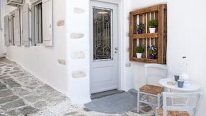 A white building with a stone-paved entrance, a wooden door with metal bars, and a small round table with chairs. - Portes View House (Paros)