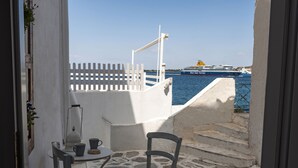 A balcony with a white railing, a table with chairs, and a view of the sea with a cruise ship in the distance. - Portes View House (Paros)