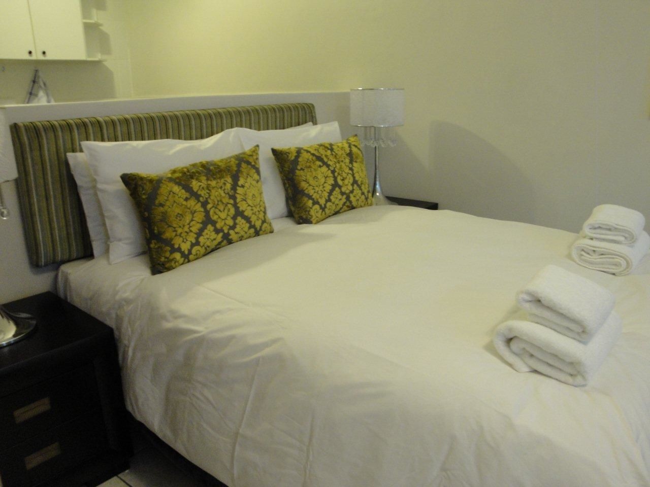 A neatly made bed with white linens, two patterned pillows, and a folded towel on the side.