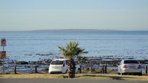 A coastal road with parked cars, a palm tree, and a clear view of the sea. - Sandringham I (Cape Town)