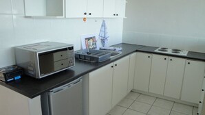 A kitchen with white cabinets, a microwave, a toaster, and a small refrigerator. - Sandringham I (Cape Town)