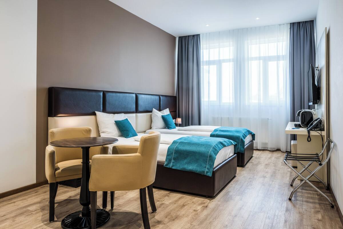 A hotel room with a bed, a desk, a chair, and a small table.