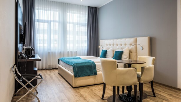A modern hotel room with a large bed, a desk with a telephone, a chair, and a small table. - RheinCity Hotel (Ludwigshafen)