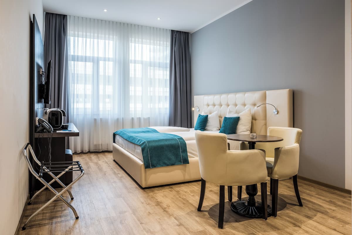 A modern hotel room with a large bed, a desk with a telephone, a chair, and a small table.