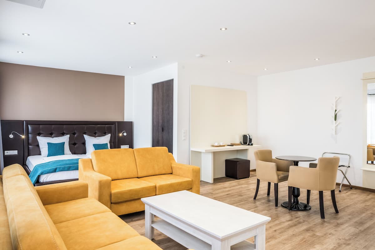A modern hotel room with a bed, sofa, and a dining area with chairs and a table.