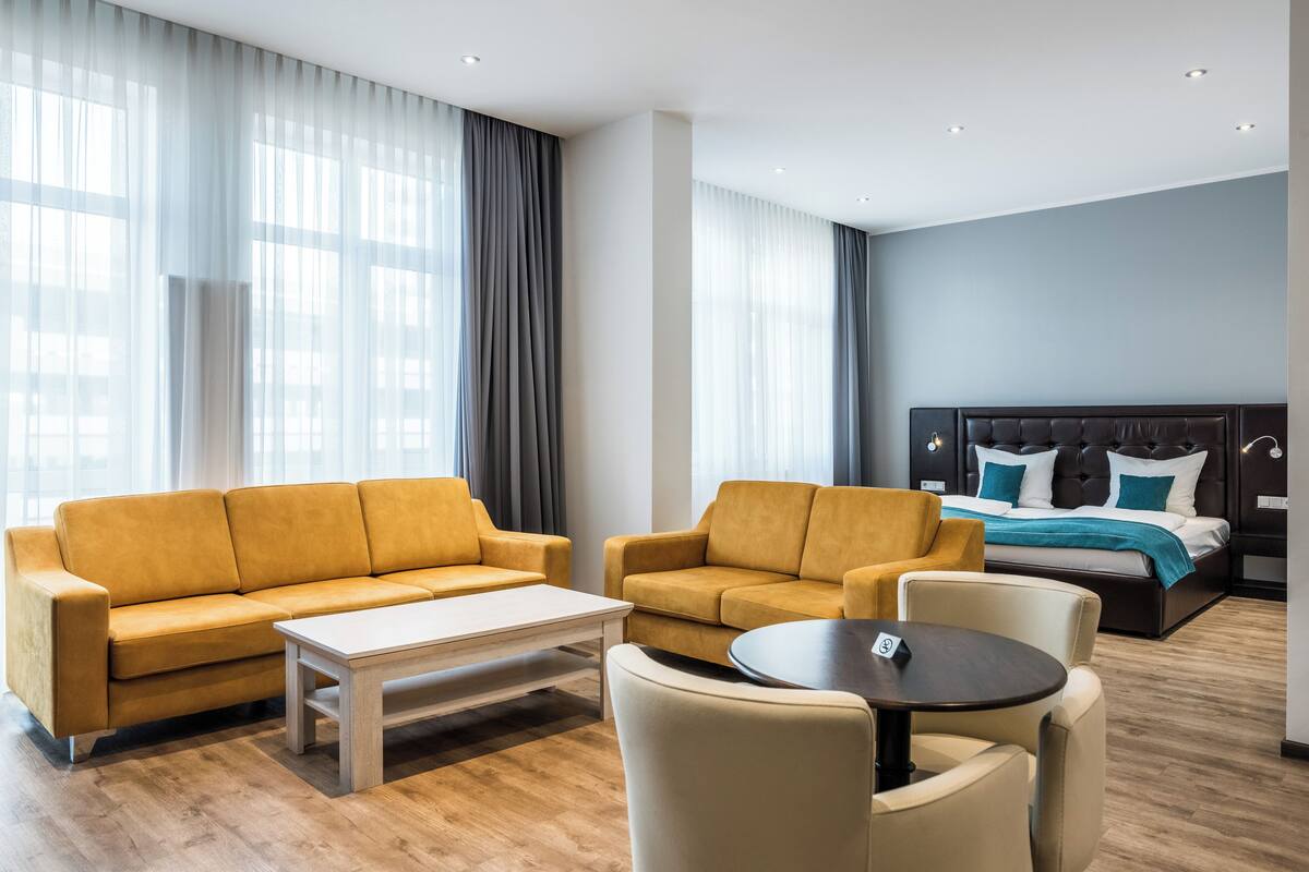 A modern hotel room with a sofa set, a coffee table, and a bed with a headboard.
