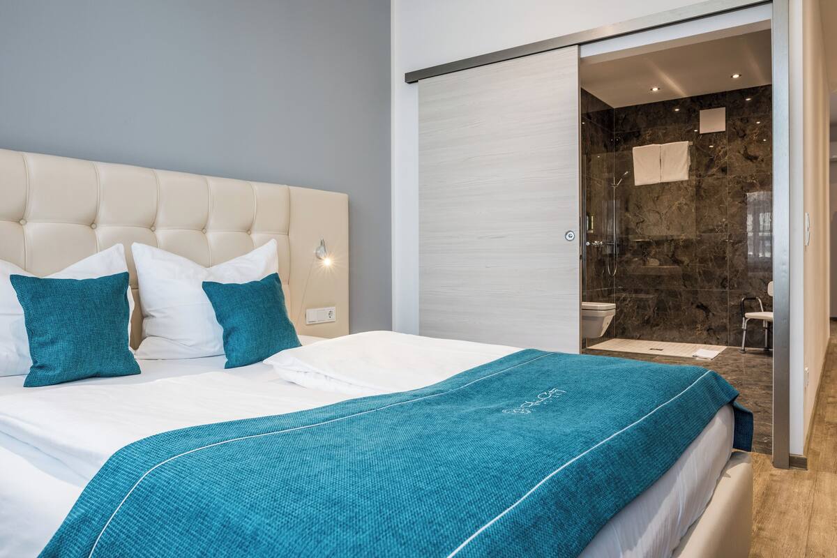 A modern hotel room with a large bed, a bathroom with a glass shower, and a sliding door leading to the shower area.