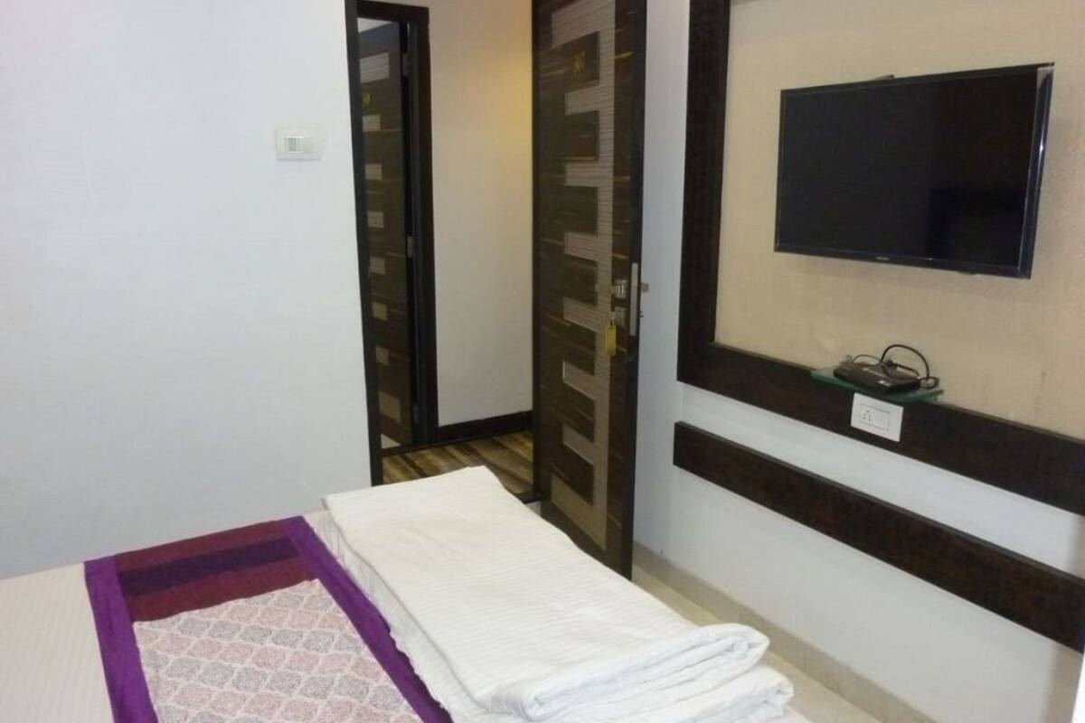 Una habitación de hotel con una cama, un televisor fijado a la pared y una puerta que da a otra estancia.