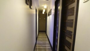 A hotel hallway with a striped carpet, dark doors, and wall-mounted lights. - Room Maangta 136 - CST (Mumbai)