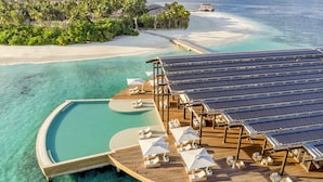 Bungalows sobre el agua con paneles solares, agua turquesa cristalina y una playa.