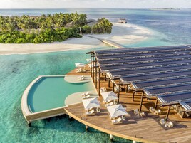 Bungalows sobre el agua con paneles solares, agua turquesa cristalina y una playa.