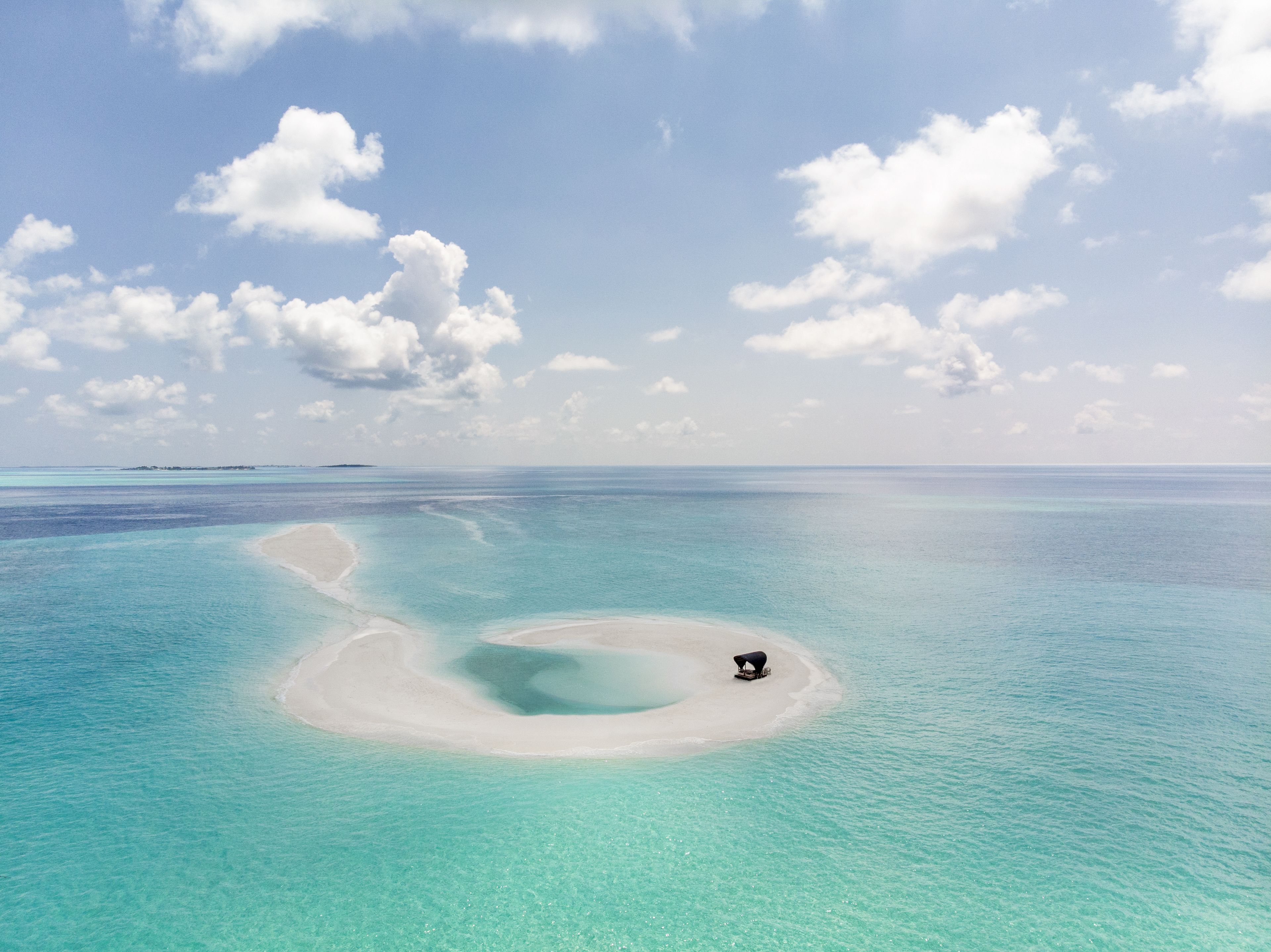 Una playa tropical con aguas turquesas cristalinas y una pequeña isla con una playa de arena blanca y una estructura oscura.