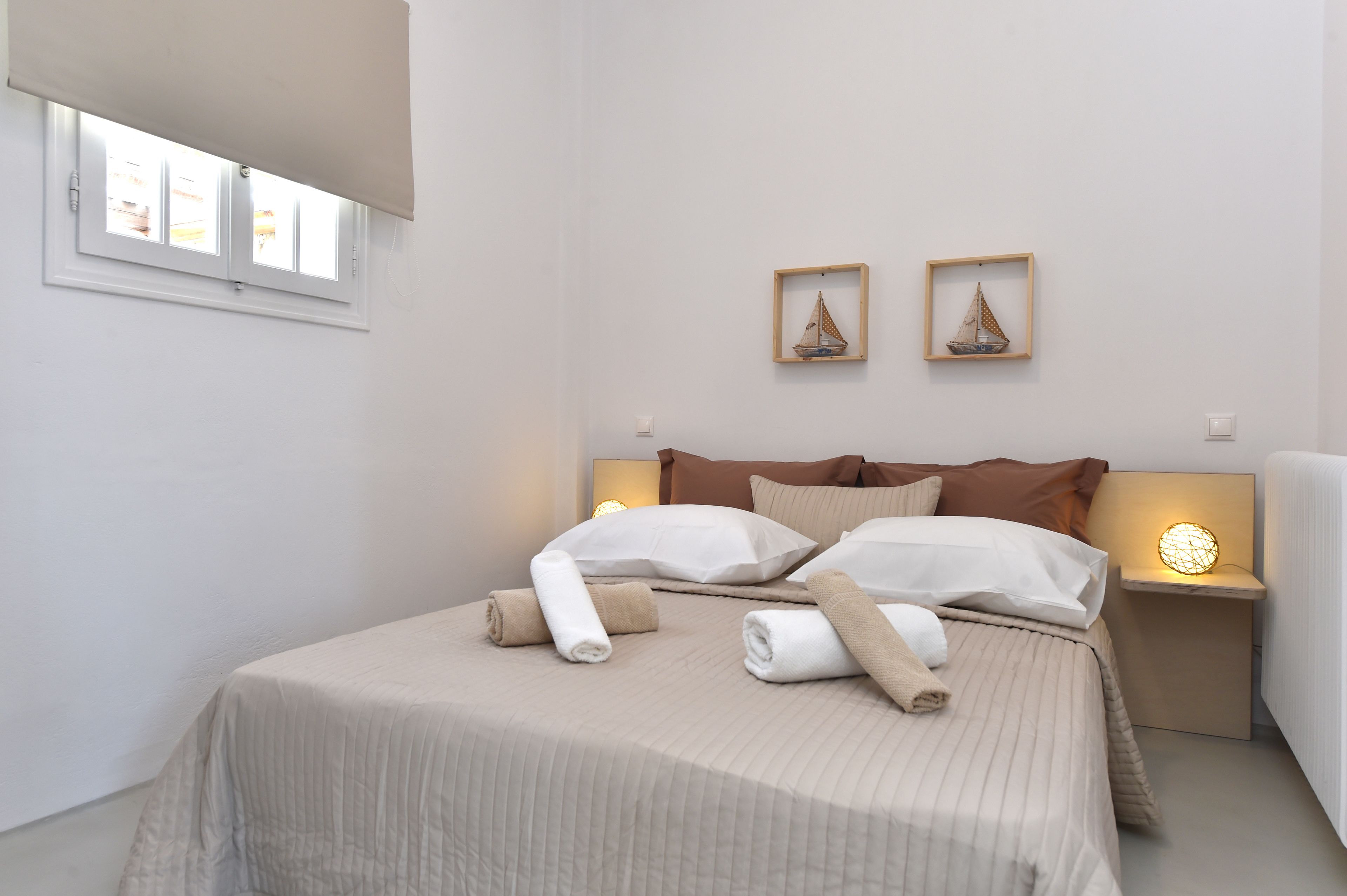 Ein ordentlich gemachtes Bett mit aufgerollten Handtüchern, zwei gerahmte Bilder an der Wand und Nachttischlampen.