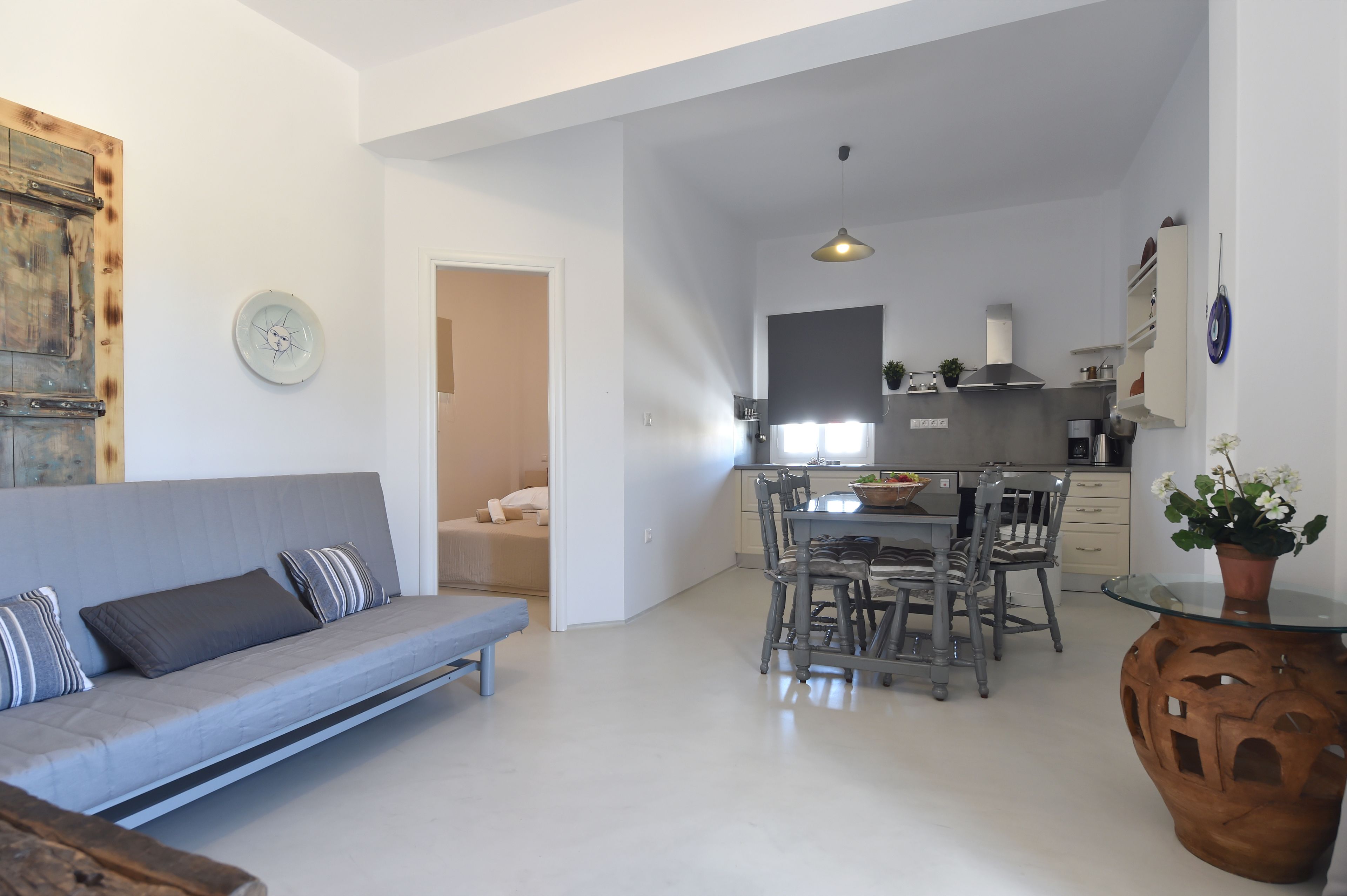 A modern living room with a grey sofa, a dining table with chairs, and a kitchen in the background.