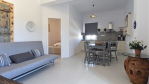 A modern living room with a grey sofa, a dining table with chairs, and a kitchen in the background. - Vagia Calm House (Paros)