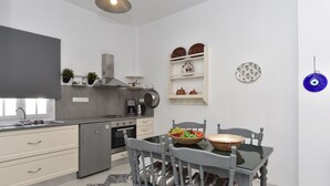 A modern kitchen with a dining area, featuring a refrigerator, stove, and a dining table with chairs. - Vagia Calm House (Paros)