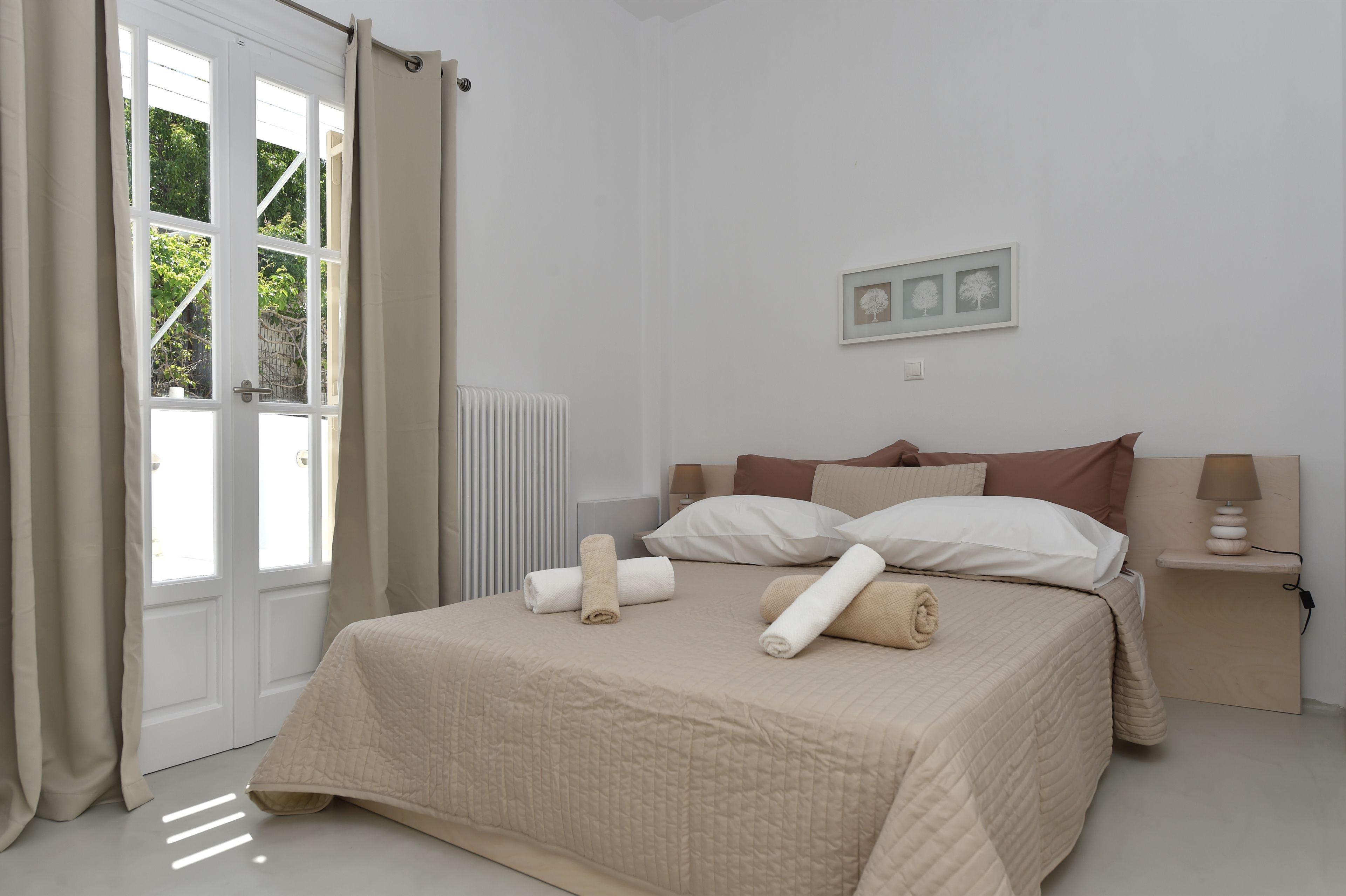 A bedroom with a bed, a bedside table with a lamp, a radiator, and a door with curtains.