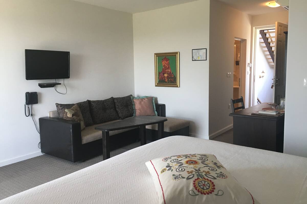 Une pièce comprenant un lit, un canapé, une petite table, un téléviseur fixé au mur et un escalier menant à un autre niveau.