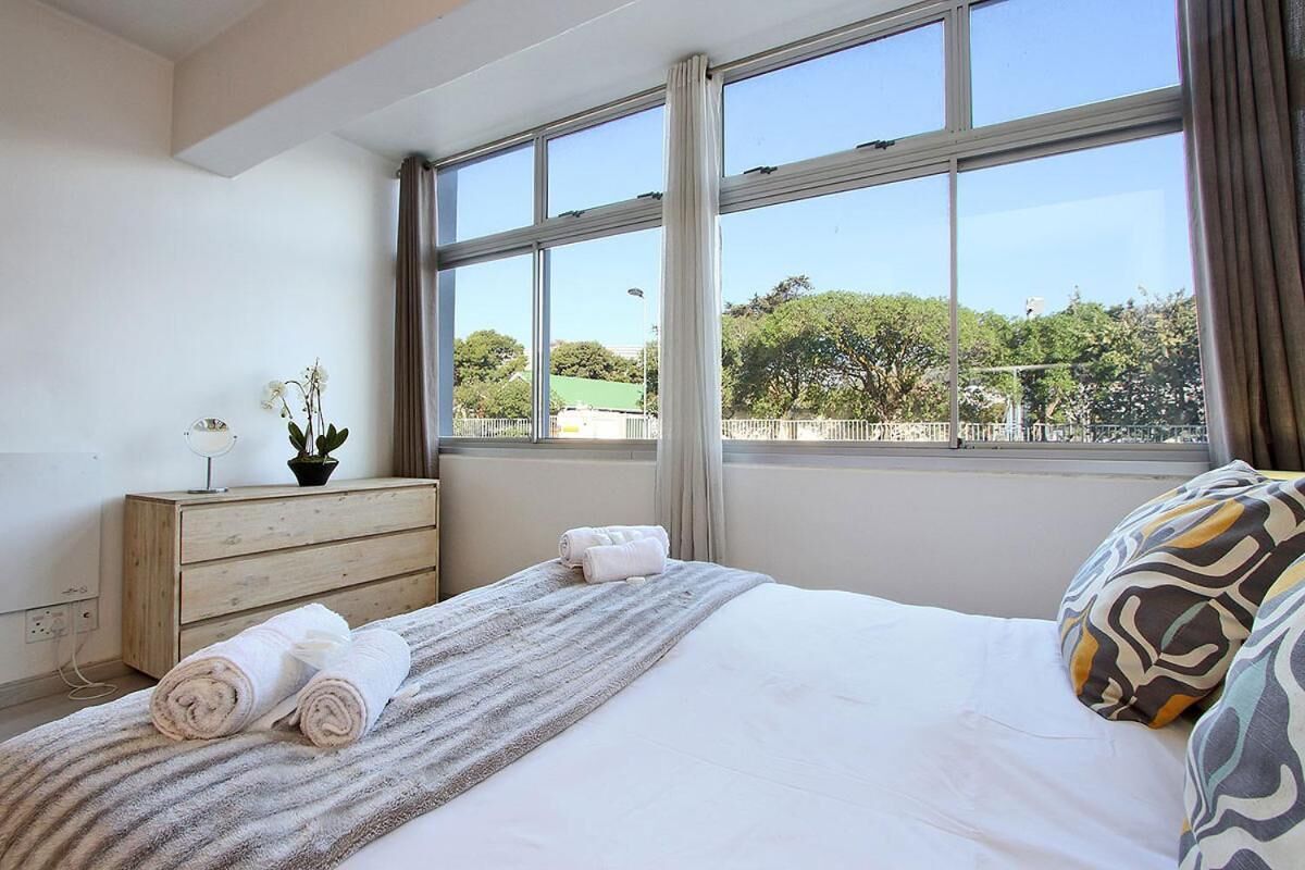 A hotel room with a bed, a dresser, a mirror, and a window with a view of trees and a fence.