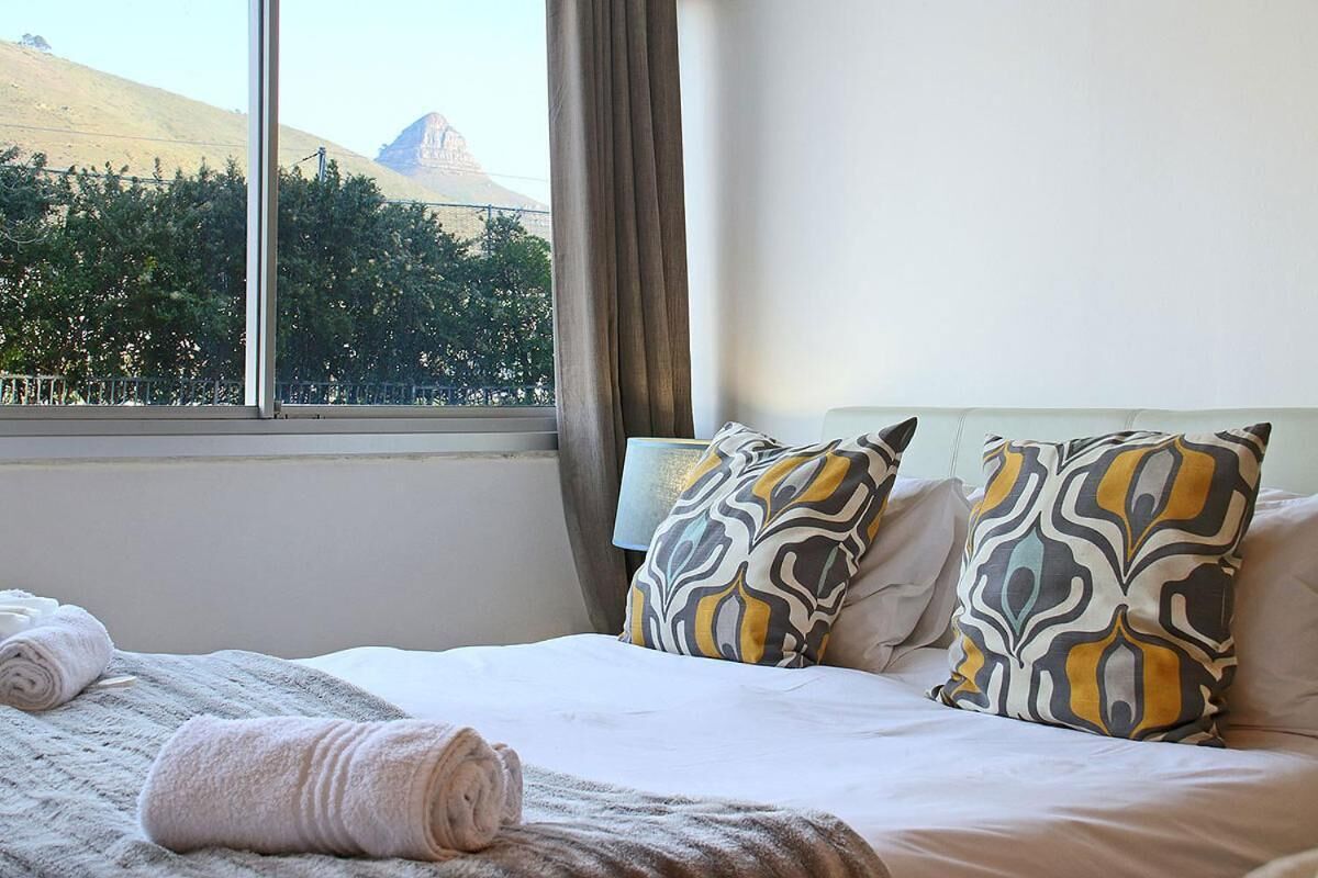 A hotel room with a bed, two patterned pillows, a window with a view of a mountain, and a towel on the bed.