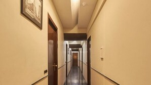 A long, narrow hotel corridor with doors on both sides, a framed picture on the left wall, and a ceiling light. - Room Maangta 213 - Juhu (Mumbai)