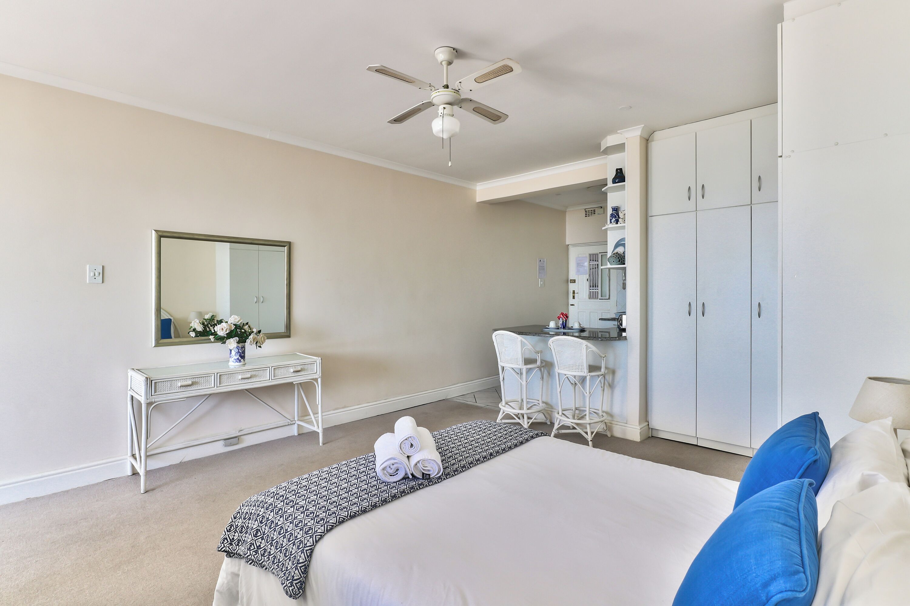 A hotel room with a bed, a desk, a chair, a wardrobe, and a ceiling fan.