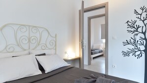 A neatly made bed with a metal headboard, a bedside table with a lamp, and a mirror reflecting a bedroom. - The Local House (Paros)