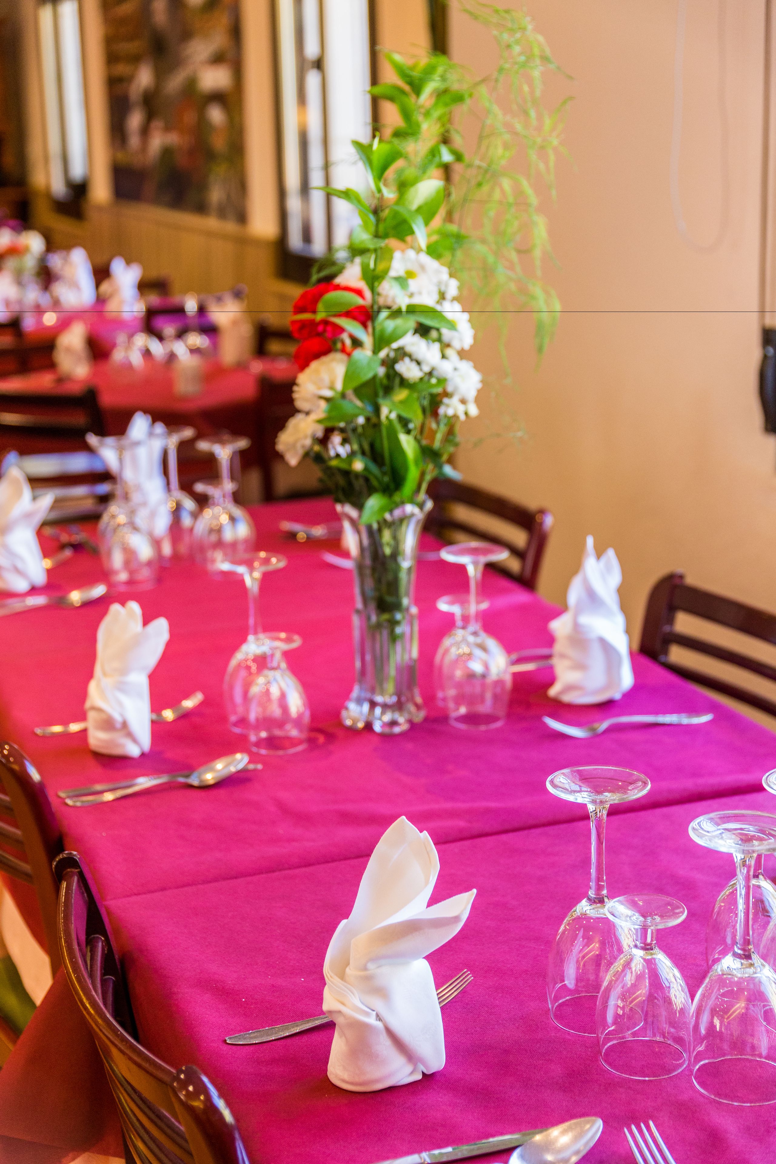 A table set for a meal with a pink tablecloth, white napkins, and clear wine glasses.