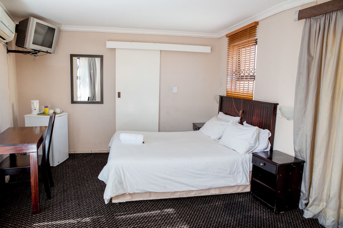 Una habitación de hotel con cama, mesita de noche, escritorio, silla, televisor y espejo.