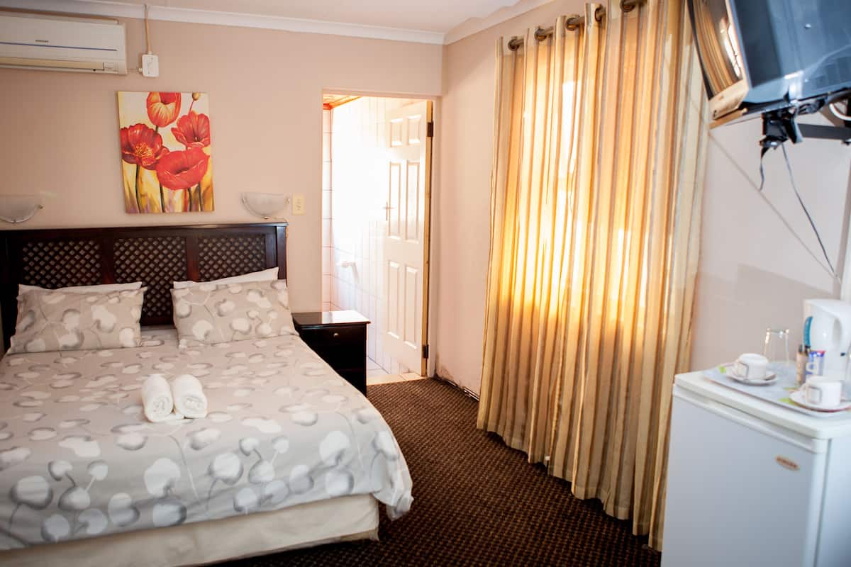 Una habitación de hotel con una cama, una mesita de noche, un televisor y una cafetera.