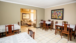 A dining area with wooden tables and chairs, a sofa, and a painting on the wall.