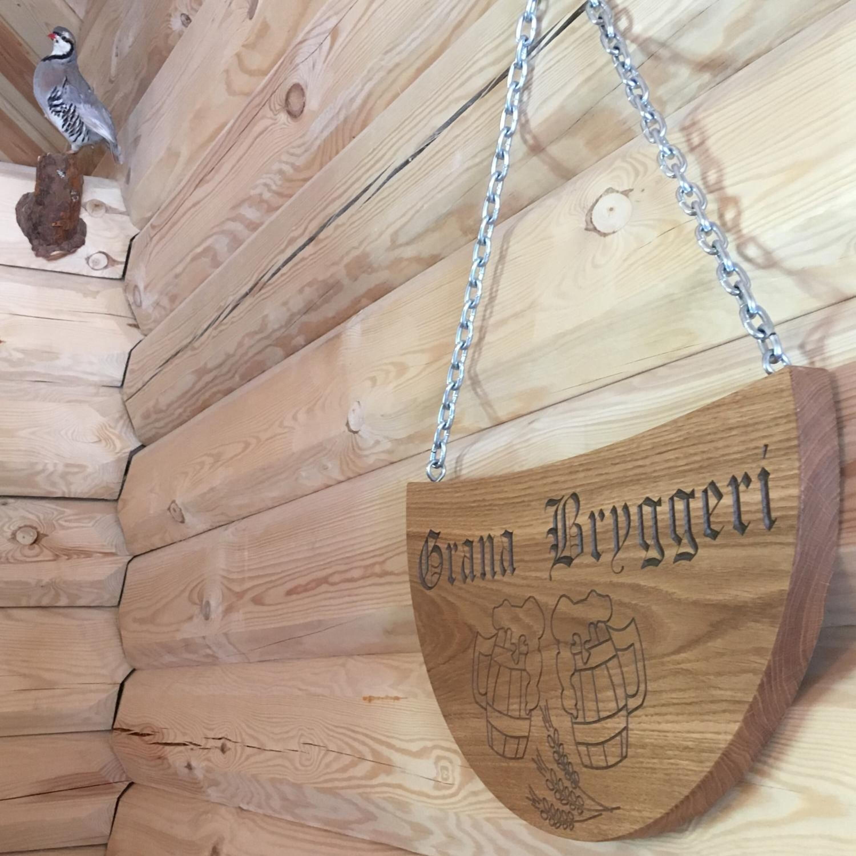 A wooden sign with the inscription "Grand Bruggeri" and a graphic of two beer mugs.
