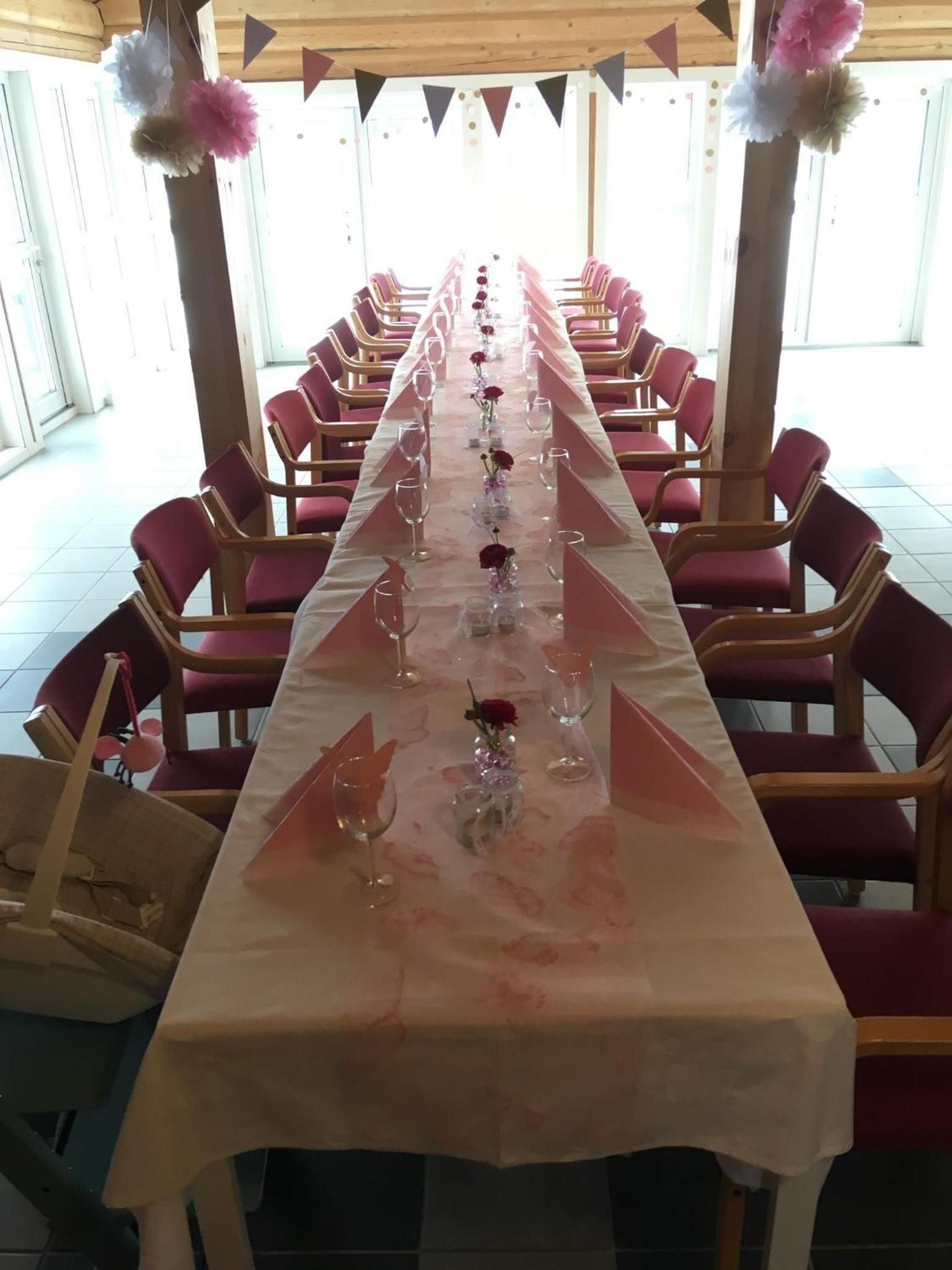 Een lange tafel met roze stoelen, ingericht voor een formeel evenement.