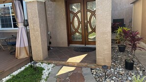 A house entrance with a wooden door, a covered patio with a table and chairs, and a garden with plants and pebbles. - Large Gorgeous home! Can sleep large groups (Long Beach)