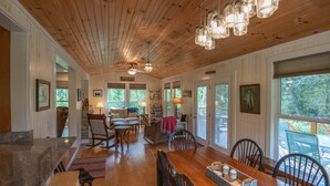 A spacious dining area with a wooden table and chairs, a kitchen area with a stone countertop, and a view of the outdoors through large windows. - Retriever Beach - New River-frontage with Your Own Private Beach! Fire Pits - Games and More! (West Jefferson)