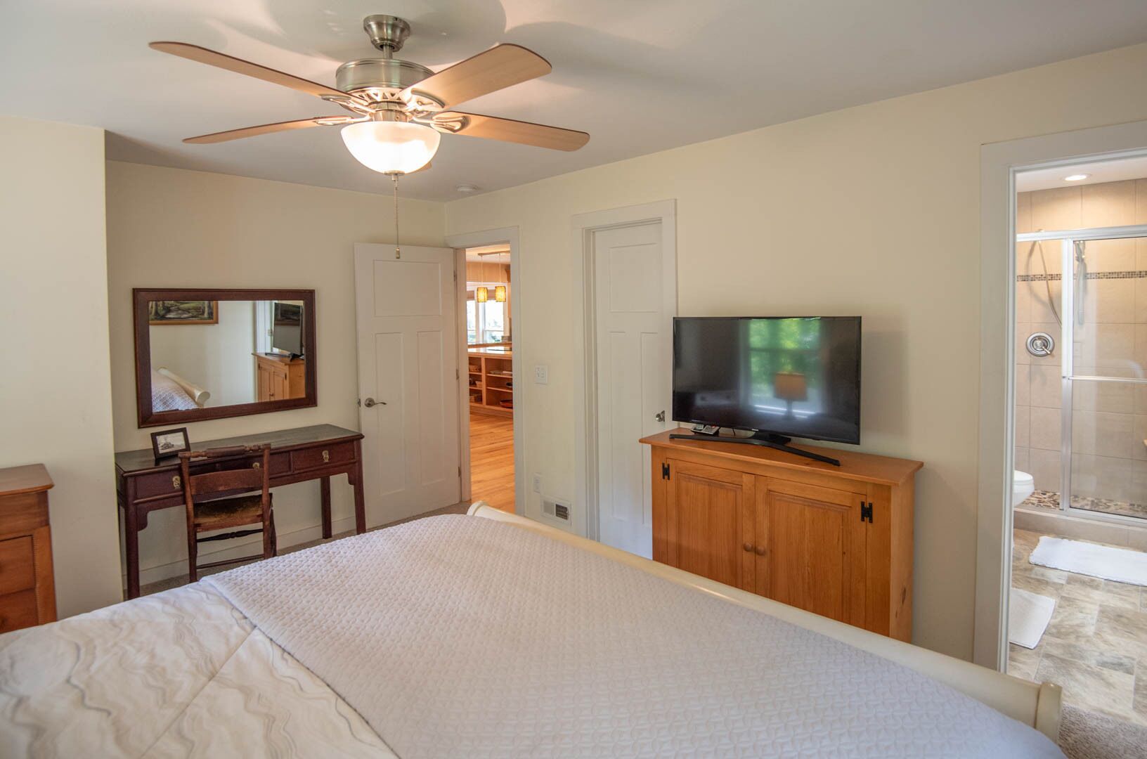 Ein Schlafzimmer mit Bett, Schreibtisch, Fernseher, Kleiderschrank und Deckenventilator.