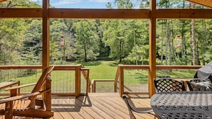 A wooden deck with a view of a forested area, a grassy lawn, and a fenced area. - Retriever Beach - New River-frontage with Your Own Private Beach! Fire Pits - Games and More! (West Jefferson)