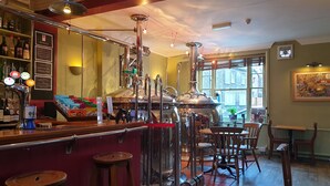 Un espace bar avec des tabourets, un comptoir avec des bouteilles et une grande structure métallique.
