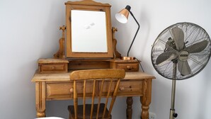 A wooden desk with a mirror, a lamp, and a standing fan.