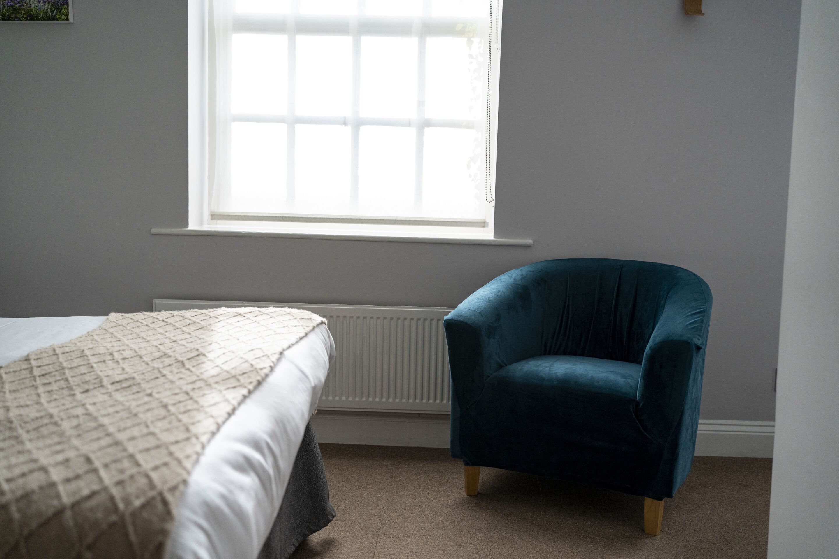 A bedroom with a bed, a window, and a blue armchair.