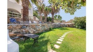A stone wall with a metal table and chairs, a grassy area with a stone path, and palm trees. - Amazing 1-Bedroom House in Tinos (Tinos)