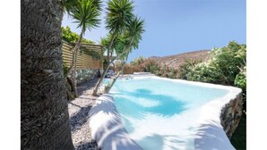 A pool with a stone edge, surrounded by trees and a wooden pergola. - Amazing 1-Bedroom House in Tinos (Tinos)
