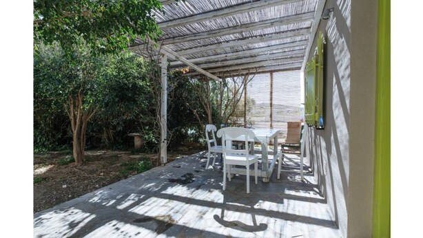 An outdoor patio with a table and chairs, surrounded by trees and a covered area. - Amazing 1-Bedroom House in Tinos (Tinos)